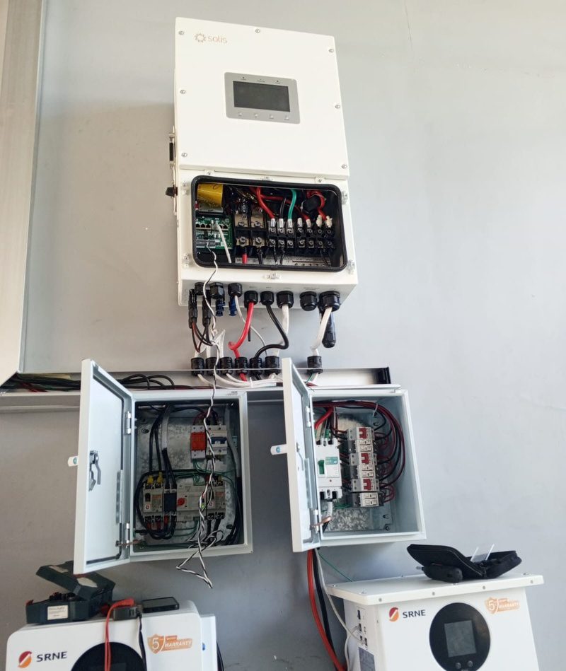 An inverter and two open protection boxes with wiring exposed for testing, batteries below.