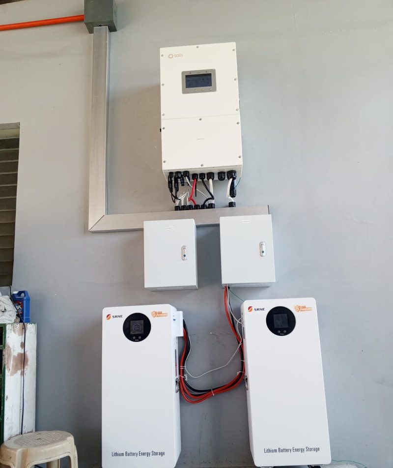 A wall-mounted hybrid inverter above two protection boxes and two floor-standing batteries.