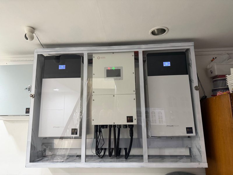 The glass-fronted cabinet straight on: battery, inverter, battery, cables dressed down through the base.