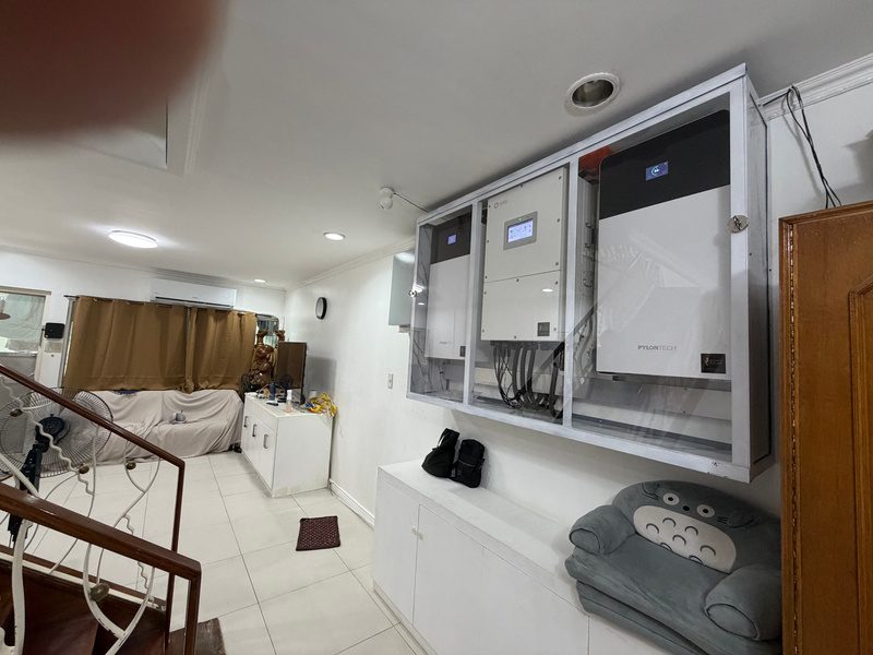 The cabinet seen from the stairs, the living room beyond, equipment screens glowing behind the glass.