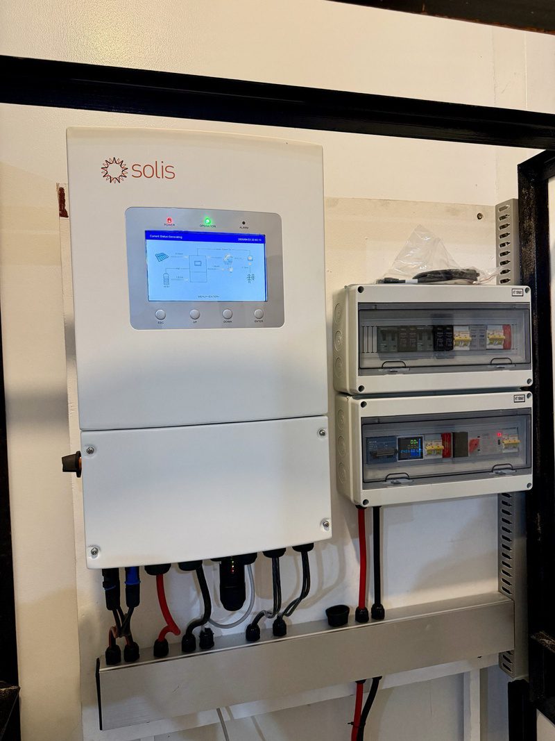A hybrid inverter with its screen reading generating, two protection boxes beside it, inside the open cabinet.