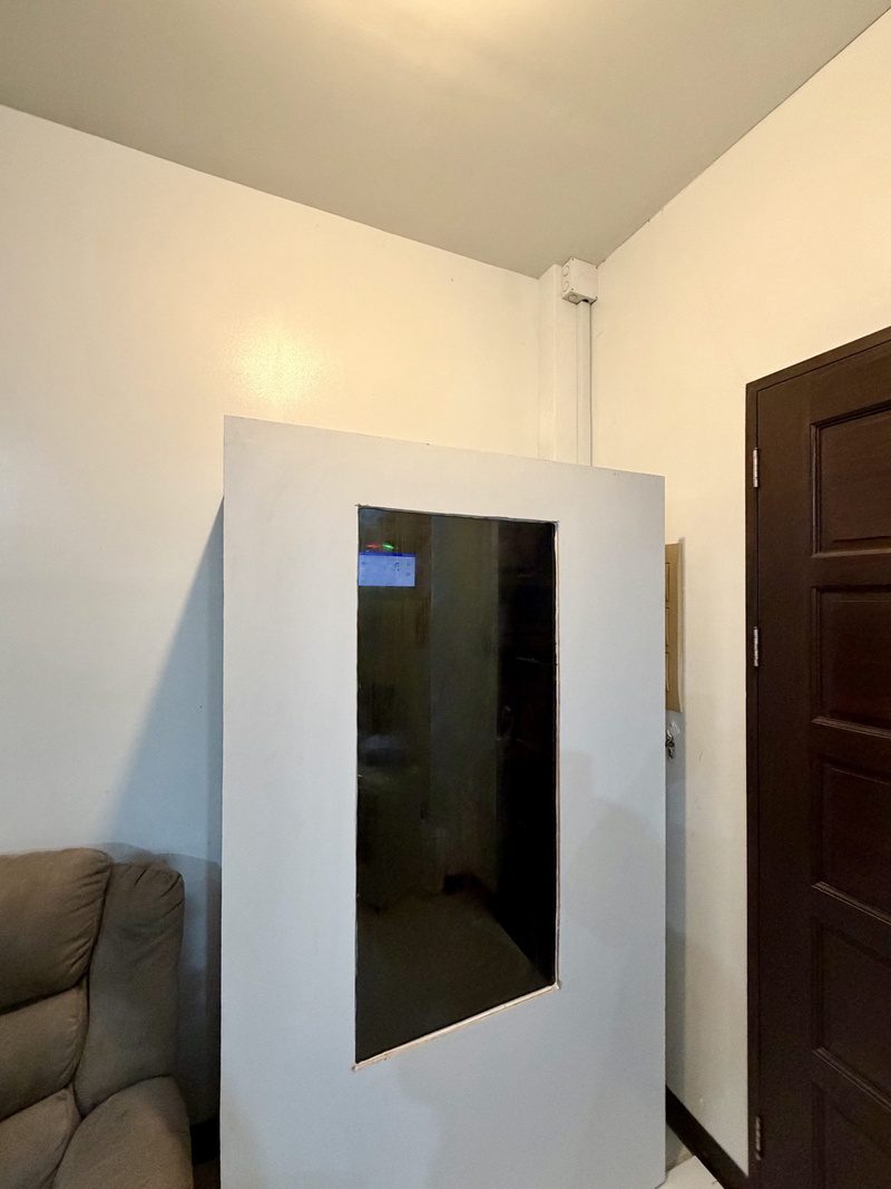 The closed white cabinet with a tinted viewing window, the inverter screen glowing through it, beside a couch.