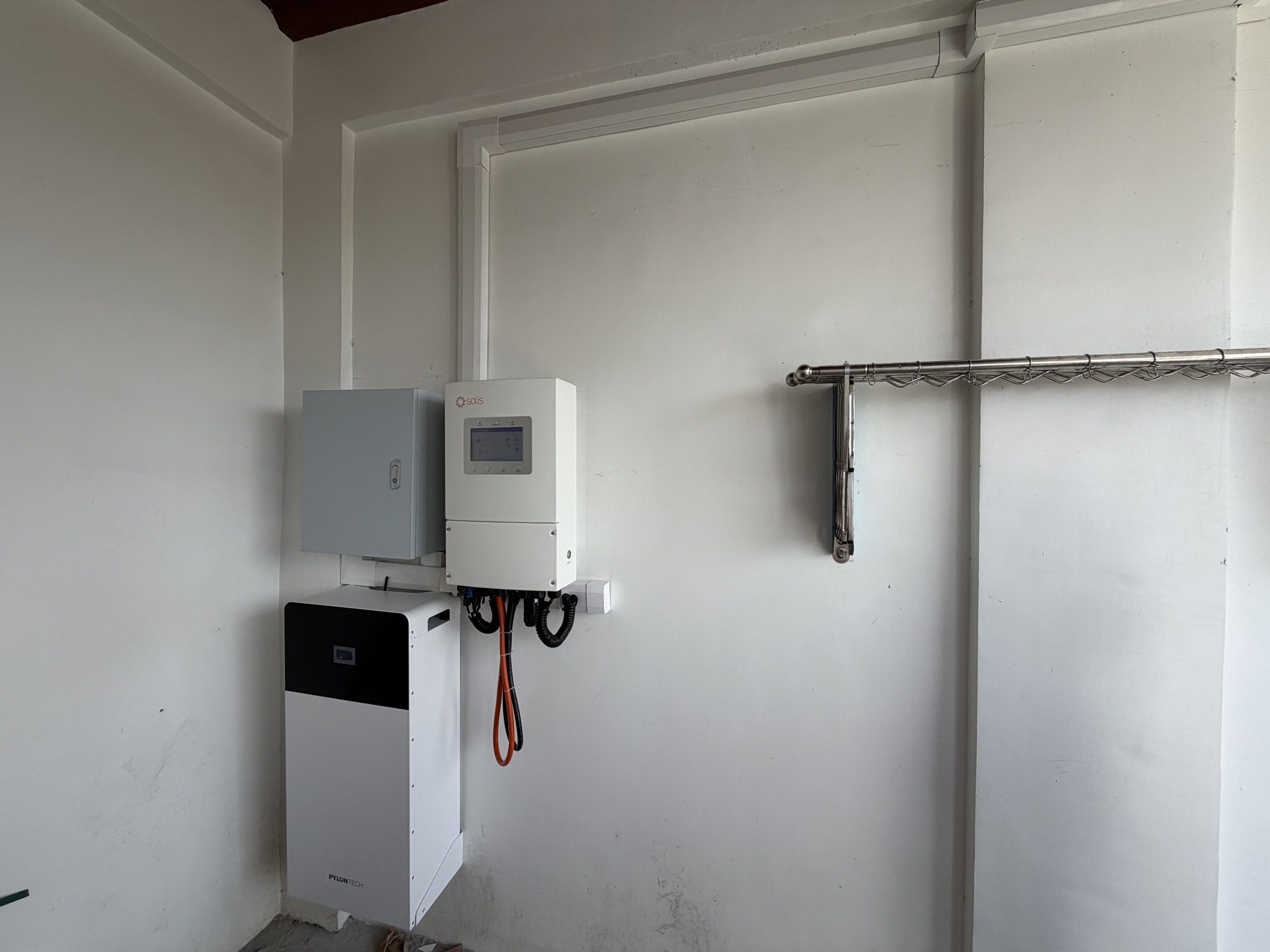 A hybrid inverter, a protection box and a floor-standing battery on a white garage wall in Malolos, cable trunking run along the wall and ceiling.
