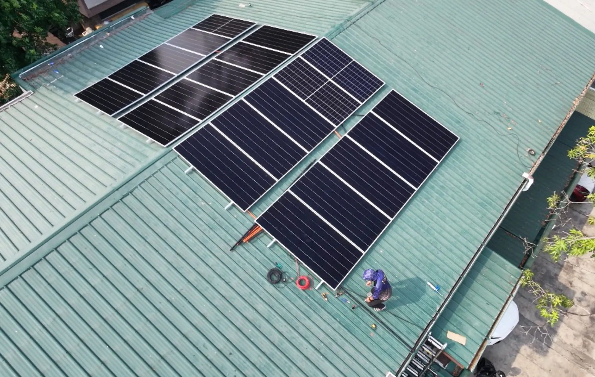 Aerial view of a finished panel array on a green corrugated roof in Mandaluyong, one installer finishing the cabling.