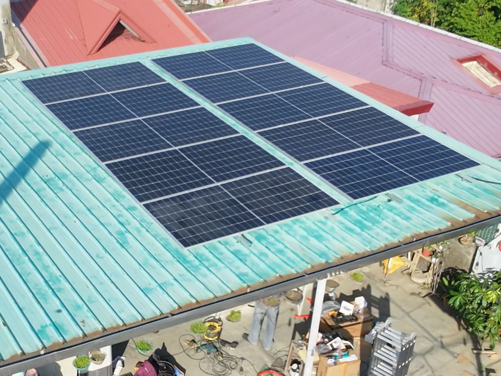 Aerial view of a new panel array on a teal metal roof over a Metro Manila roof deck, neighbouring roofs on every side.